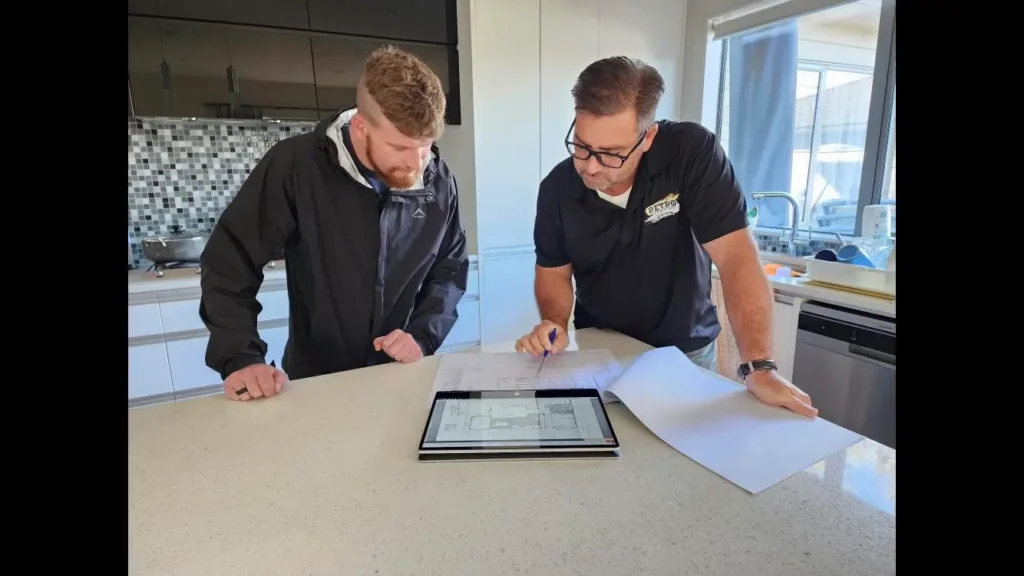 Two men reviewing kitchen remodel plans on a tablet and paper in a modern kitchen. Kitchen design, renovation project.