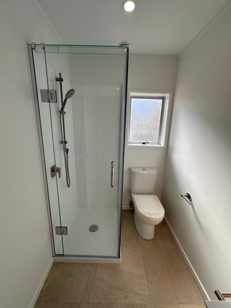 Bathroom interior with glass shower, toilet, and small window. Modern bathroom design for January 2026 newsletter.