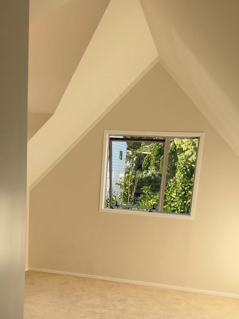 Attic room interior in January 2026 newsletter, featuring window view of lush greenery, natural light, and neutral decor.