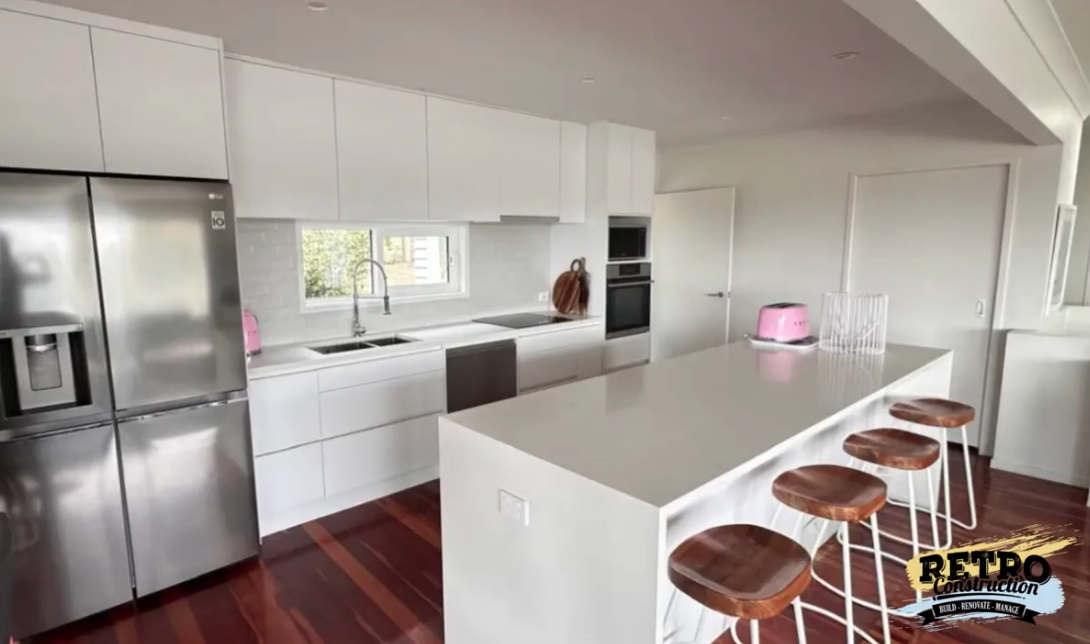 Modern kitchen showcase with white cabinets, stainless steel appliances, and a large island with seating. Kitchen renovation.