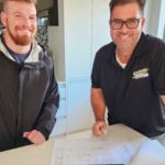 Retro Construction: Two smiling men reviewing blueprints in modern kitchen. Construction, renovation, and remodeling services.