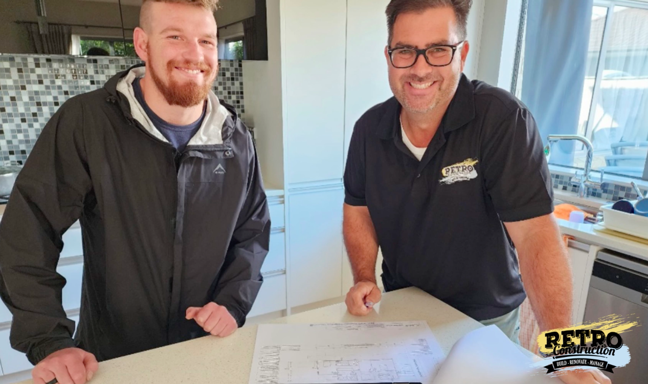 Retro Construction: Two smiling men reviewing blueprints in modern kitchen. Construction, renovation, and remodeling services.